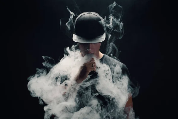 Vape adam. Bir modern siyah kap vaping ve Elektronik Sigara Buhar puffs kapalı icar yakışıklı genç bir beyaz adam portresi