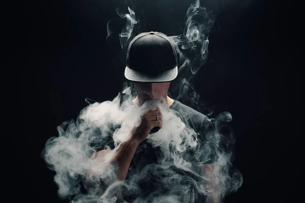 Vape adam. Bir modern siyah kap vaping ve Elektronik Sigara Buhar puffs kapalı icar yakışıklı genç bir beyaz adam portresi