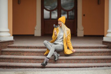 Moda portre harika kız sarı palto ve şapka ile sonbahar şehirde eğleniyor lolipop Siyah yarasa