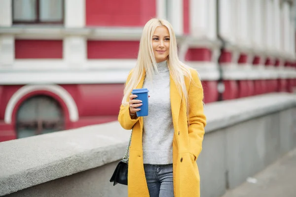노란색 코트를 그녀는 커피를 하고있다 그리고 이야기 거리에 전화에 여자의 — 스톡 사진