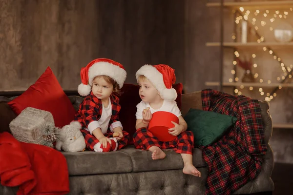 戴着圣诞老人帽子的可爱的小孩子 坐在客厅里的一张容易放的大椅子上 在盒子里看圣诞礼物 — 图库照片