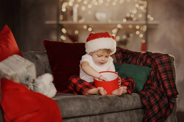 一个戴着圣诞老人帽子的小孩男孩坐在柔软的家里沙发上 吃红色盒子里的饼干 圣诞节家庭假日 — 图库照片