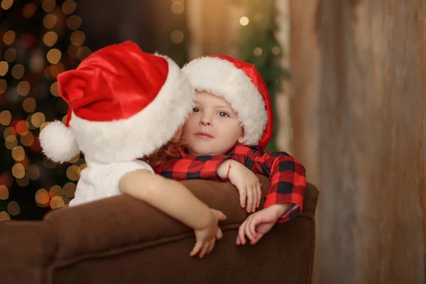 两个戴着圣诞老人帽子的可爱的小孩子坐在柔软的家里沙发上玩得很开心 家庭圣诞节假期 — 图库照片