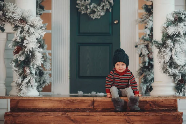 Cute child boy sits on the porch of the magic house of Santa Claus. Miracle time. Merry Christmas and Happy New Year