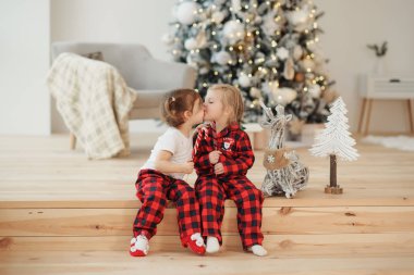 İki küçük kız kardeş kırmızı pijama Noel sabahı oturma odasında oturup tatlılar yemek. Aile Partisi, hugs ve öper