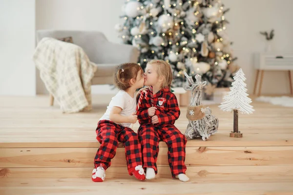 圣诞节早上 两个穿着红色睡衣的小妹妹坐在客厅里吃糖果 家庭聚会 拥抱和亲吻 — 图库照片