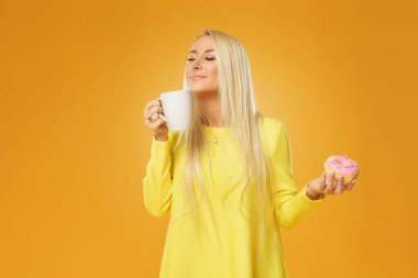 Çörek ve kahve yüzünü sarı arka plan üzerinde izole, poz sarı elbiseli bir gülümseyen kız portresi kapatın