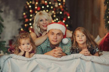 Mutlu Noeller ve mutlu tatiller! Neşeli veliler ve ve eğleniyor ve birlikte oturma odasında yatağın üstünde Noel ağacının yanında oynayan iki küçük çocuk