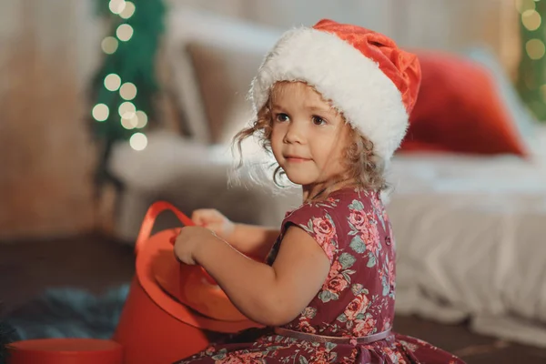 可爱的小女孩坐在圣诞树附近 看着里面发光的圣诞礼品盒 — 图库照片