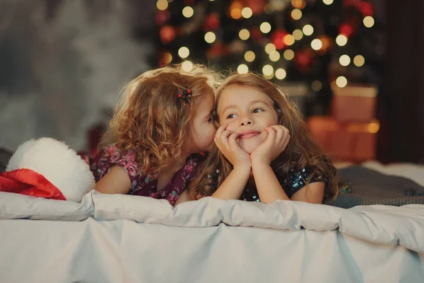两个戴着圣诞老人帽子的可爱姐妹坐在一个柔软的家 背景是一个节日圣诞树拥抱和微笑 家庭家庭新年假期 子女关系 — 图库照片
