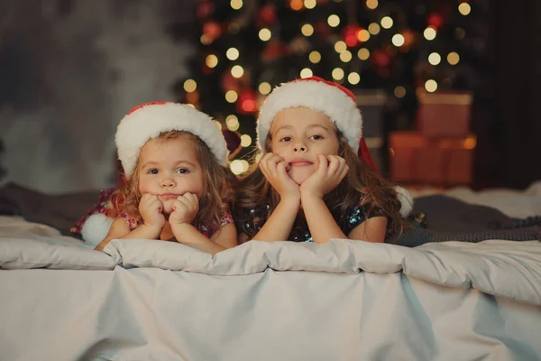 Two Cute Sisters Santa Claus Hats Sitting Soft Home Bad — Stock Photo, Image