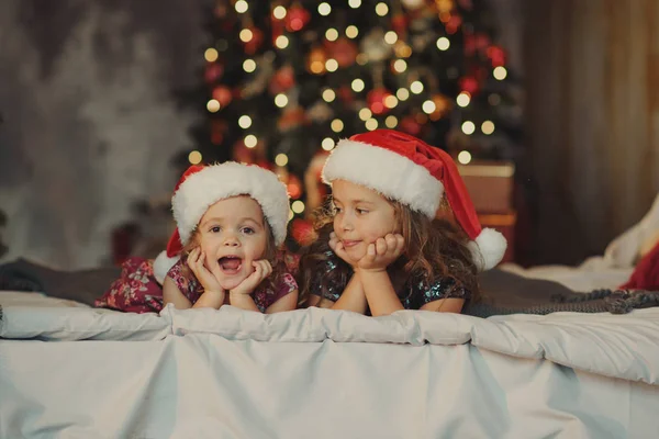 Two Cute Sisters Santa Claus Hats Sitting Soft Home Bad — Stock Photo, Image