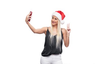 Gülümseyen mutlu sarışın kadın siyah bluz ve Noel şapka selfie kırmızı smartphone kamera üzerinden yapmak Noel Baba beyaz arka plan izole. Satış konsepti