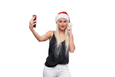 Gülümseyen mutlu sarışın kadın siyah bluz ve Noel şapka selfie kırmızı smartphone kamera üzerinden yapmak Noel Baba beyaz arka plan izole. Satış konsepti