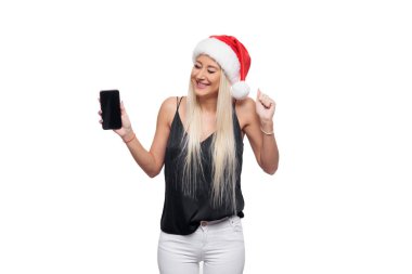 Sürpriz sarışın kadın siyah bluz ve Noel Noel Baba şapkası elini ve kameraya izole beyaz arka plan üzerinde arıyor bir akıllı telefon üzerinde bir parmak gösterir. Satış konsepti