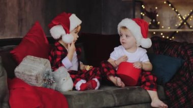 Genç çocuk, kardeşi ve kız kardeşi, Noel Baba şapkaları Noel ağacının altına oturma odasında oturmak ve hediyeleri açalım. Oda ışık ampuller ile geleneksel dekorasyon. Aile kavramı