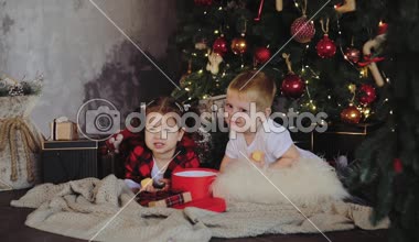 Genç çocuk, kardeşi ve kız kardeşi, Noel Baba şapkaları Noel ağacının altına oturma odasında oturmak ve hediyeleri açalım. Oda ışık ampuller ile geleneksel dekorasyon. Aile kavramı