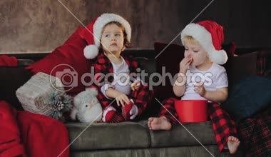 Genç çocuk, kardeşi ve kız kardeşi, Noel Baba şapkaları Noel ağacının altına oturma odasında oturmak ve hediyeleri açalım. Oda ışık ampuller ile geleneksel dekorasyon. Aile kavramı
