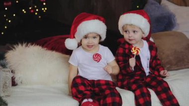 Noel Baba şapkaları Noel ağacının altına oturma odasında oturup, küçük çocuklar ve kız ve açık sunar ve şeker yiyor. Aile kavramı
