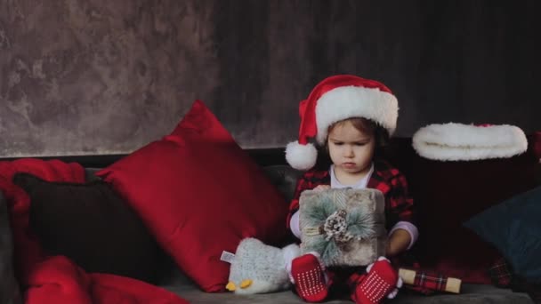 孩子拿着打开一个圣诞礼品盒 戴着圣诞老人的帽子 孩子在家里玩得很开心 圣诞节寒假概念 — 图库视频影像
