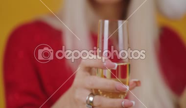 Mutlu heyecanlı genç sarışın kadın sarı arka plan üzerinde hediye kutusu ile Noel Baba şapkalı. Bir partide pahalı şampanya içme