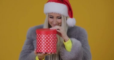 Mutlu güzel gülümseyen kadın kürk manto ve Noel Baba şapkası sarı zemin üzerine kırmızı hediye kutusunu açma. Noel kutlamak, wow efekti ve sürpriz