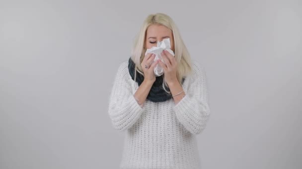 白い背景にくしゃみがニット暖かいスカーフで病気の金髪女性 — ストック動画