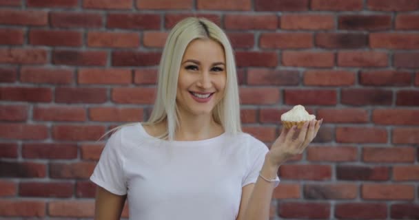 食欲と喜びと白い シャツを着た若い金髪女性がクリームとケーキを食べます — ストック動画