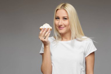 Sarışın kadın gri bir arka plan üzerinde izole pasta yemeye gülüyor. Diyet yok