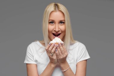 Sarışın kadın gri bir arka plan üzerinde izole pasta yemeye gülüyor. Diyet yok