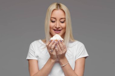 Sarışın kadın gri bir arka plan üzerinde izole pasta yemeye gülüyor. Diyet yok