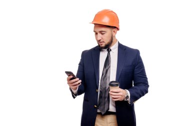 Sürpriz yüklenici ve geliştirici, telefonu hakkında konuşurken iş portre. Baret fincan kahve ayakta beyaz arka plan üzerinde işadamı. Haber ve kahve fren kavramı