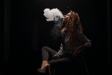 Kızıl saçlı kadın vaping elektronik sigara duman siyah arka plan ile. Genç kadın e-sigara tütün çıkmak için. Buharı ve alternatif nikotin ücretsiz Sigara kavramı kopya alanı 