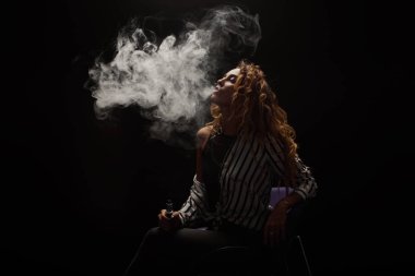 Kızıl saçlı kadın vaping elektronik sigara duman siyah arka plan ile. Genç kadın e-sigara tütün çıkmak için. Buharı ve alternatif nikotin ücretsiz Sigara kavramı kopya alanı 