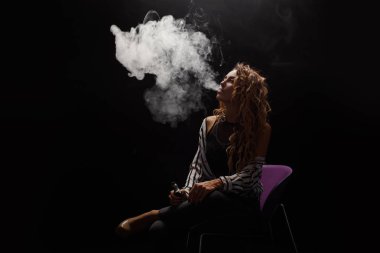 Kızıl saçlı kadın vaping elektronik sigara duman siyah arka plan ile. Genç kadın e-sigara tütün çıkmak için. Buharı ve alternatif nikotin ücretsiz Sigara kavramı kopya alanı 