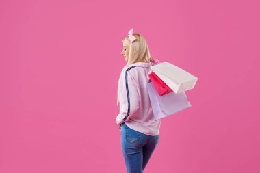 Pembe arka plan üzerinde alışveriş torbaları ile poz mutlu genç sarışın bir kadın görüntüsü. Alışveriş kavramı. Metin için yer kopyalayın