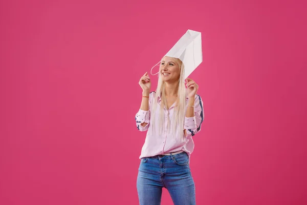 ショッピング バッグ ピンク背景の上の頭の上に 興奮して楽しいブロンドの女の子の肖像画 — ストック写真