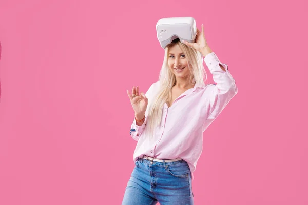 バーチャル リアリティによって若い金髪の幸せな女学生のゴーグルします ピンクの背景で撮影スタジオ 仮想学習 — ストック写真