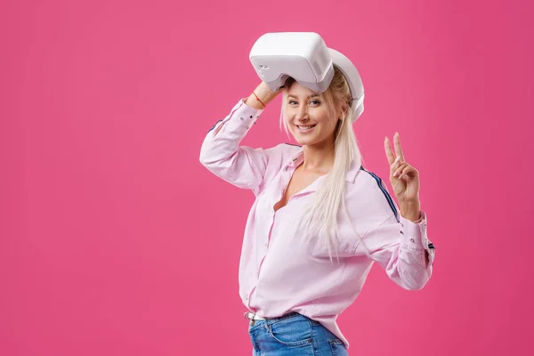 バーチャル リアリティによって若い金髪の幸せな女学生のゴーグルします ピンクの背景で撮影スタジオ 仮想学習 — ストック写真