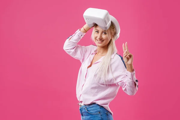 Young Blond happy woman student with virtual reality goggles. Studio shot on pink background. Virtual learning