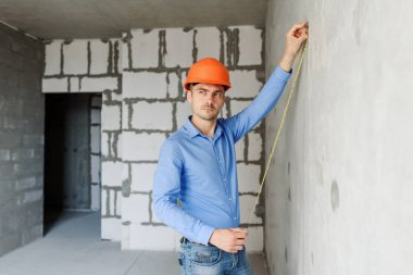 Memnun inşaat işçisi foreman bir mezura yapım aşamasında bir evde bir duvar parametrenin ölçer. Onarım hazırlık ve gerçekleşen çalışma doğruluğunu inceler