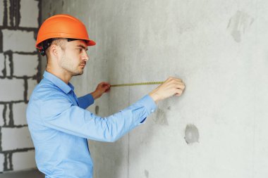 Memnun inşaat işçisi foreman bir mezura yapım aşamasında bir evde bir duvar parametrenin ölçer. Onarım hazırlık ve gerçekleşen çalışma doğruluğunu inceler