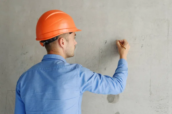 Satisfied construction worker foreman measures a tape measure of a wall parameter in a house under construction. Inspects repair readiness and accuracy of work performed