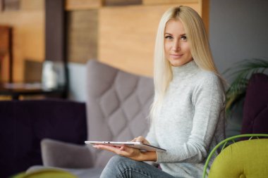 Okuma kavramı. Tablet ve içme kahve kullanan genç sarışın kadın. Rahat kafede dinlendirici, sandalyeye otur