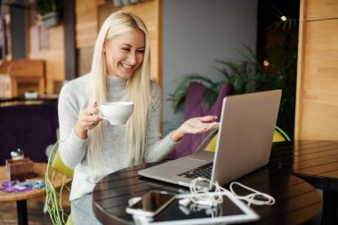 İş yerinde yoğunlaşmıştır. Yaratıcı office veya kafe pencere yanında otururken dizüstü bilgisayarda çalışan akıllı rahat kıyafet kendine güvenen genç kadın. Bir fincan kahve holding