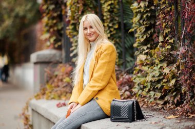 Açık moda sonbahar park veya sokak parlak sarı montlu genç sarışın bir kadın portresi