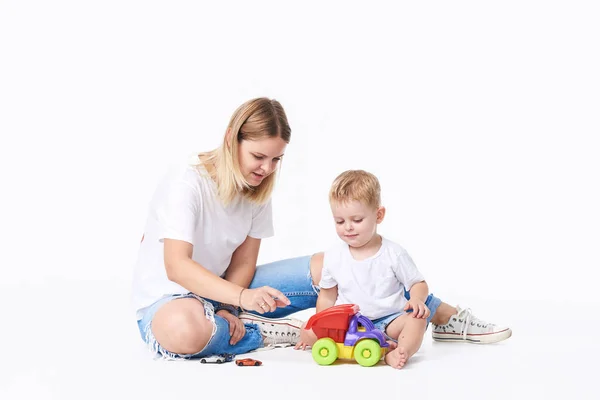 母亲的概念 年轻的妈妈和儿子玩塑料玩具和汽车 兴奋的学龄前儿童与他微笑的母亲或幼儿园老师一起玩耍 在白色上隔离 — 图库照片