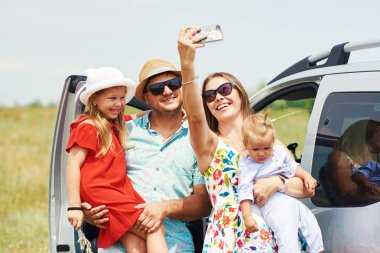 Tatil, seyahat - mutlu aile yaz tatili için seyahat için hazır. İnsanlar eğlenmek ve telefonda fotoğraf çekmek. Bir selfie almak yolculuk bellek üzerinde