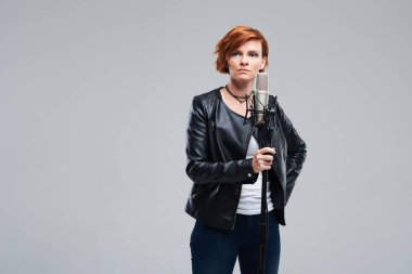 Rock şarkıcı giyen deri ceket ve statik mic, tutmak portre gri arka plan üzerine bir şarkı söylüyor. Rock müzik ve rave kavramı