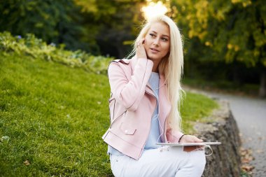 Gülümseyen yakışıklı kadın onun cep telefonu ya da tablet vasıl belgili tanımlık park Kulaklığımda rahatlatıcı müzik dinlemek. Bir öğrenci için bir online ders dinler ve sınavları için hazırlar. yalnızlık zevk kız